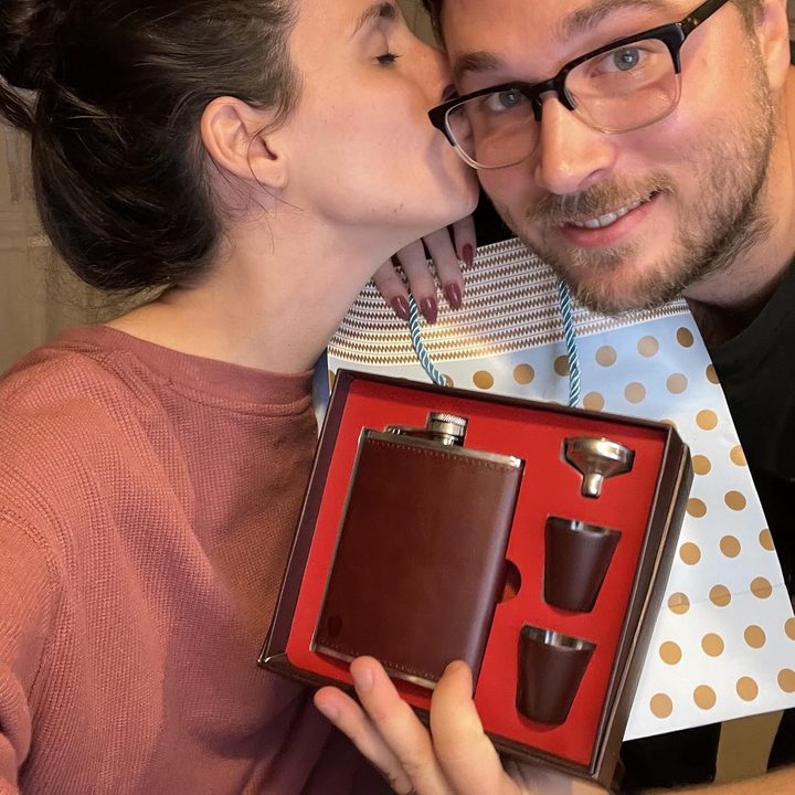 A couple holding the open gift box with the flask, cups and funnel